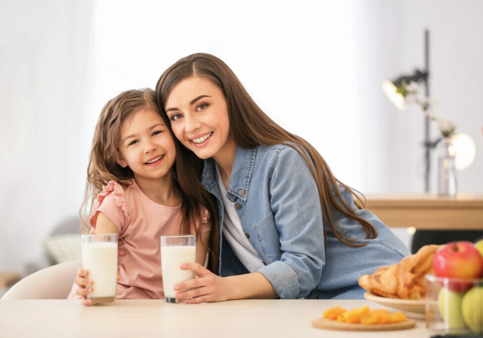 Mother and daughter having breakfast with milk at table